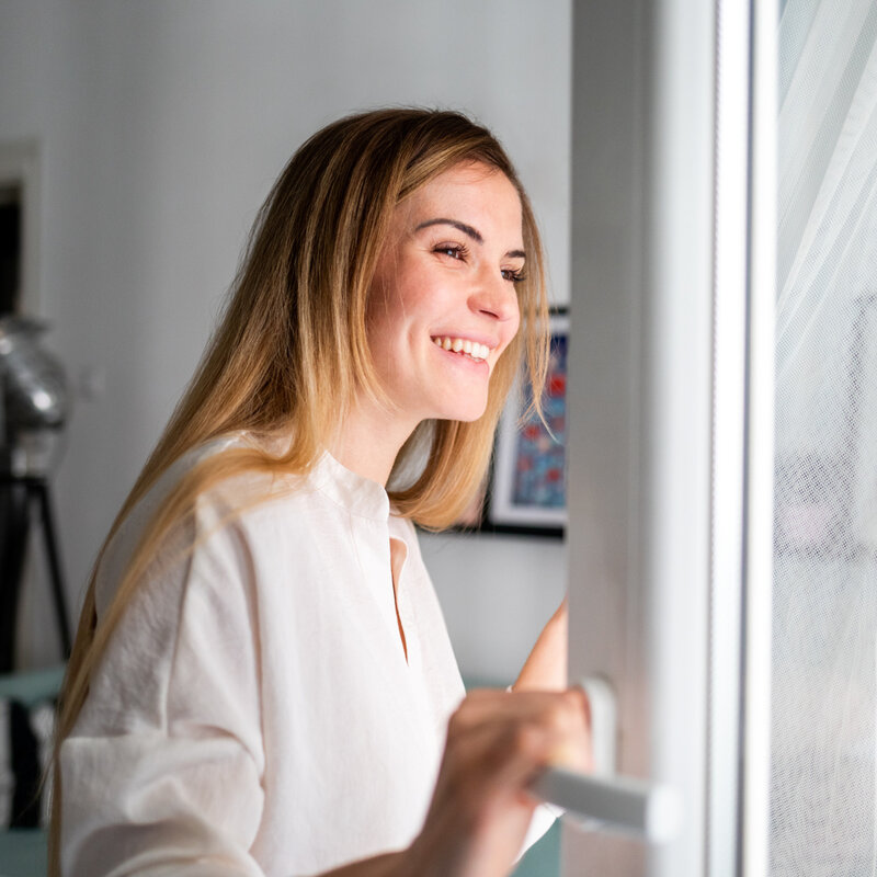 Beautiful smiling young woman opening window at the morning, fresh air, 