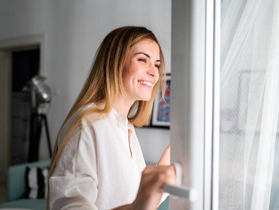 Uśmiechnięta młoda kobieta otwierająca okno o poranku po świeże powietrze
