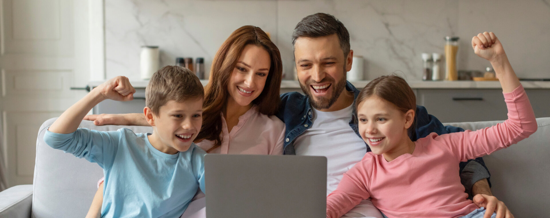 Happy family with two children sitting on a couch and celebrating as they look at a laptop screen at home
